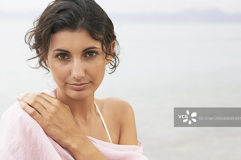 年轻女人在海滩上，戴着粉色披肩，特写肖像图片素材