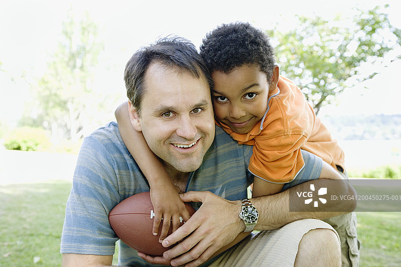 公园里，父亲和儿子（8-10岁）踢足球，微笑，肖像图片素材