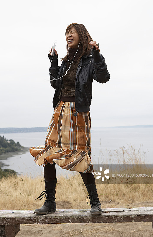 在公园长椅上戴着MP3跳舞的微笑少女（15-17岁）图片素材