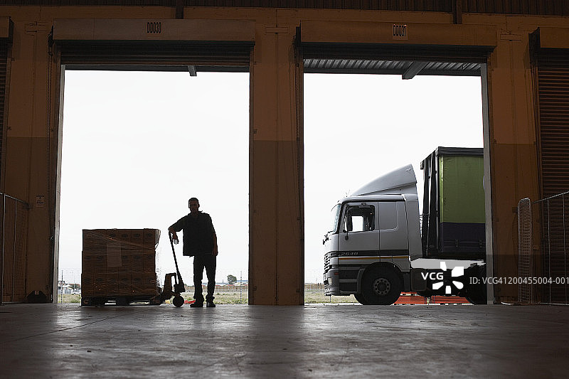 站在仓库入口处托盘交付物旁的男人图片素材