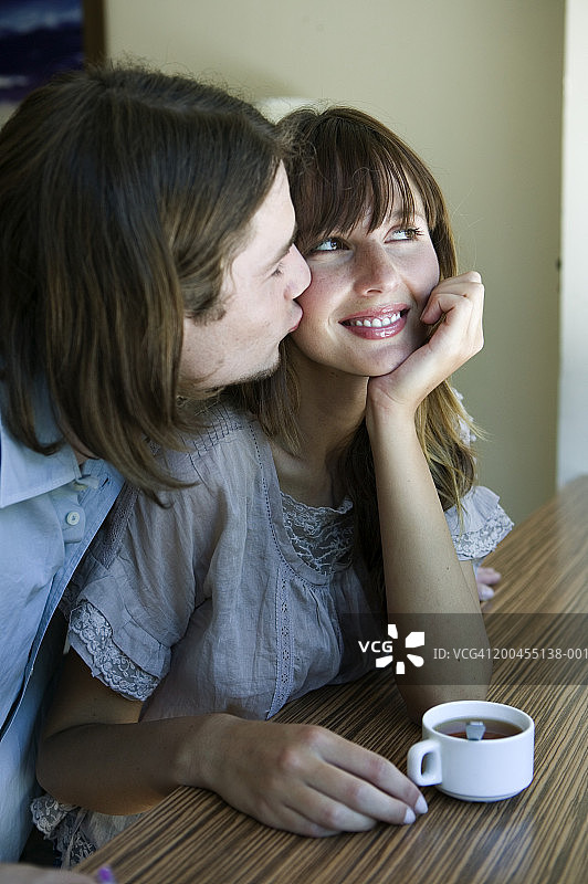 年轻男人在咖啡馆亲吻女人的脸颊，面带微笑图片素材
