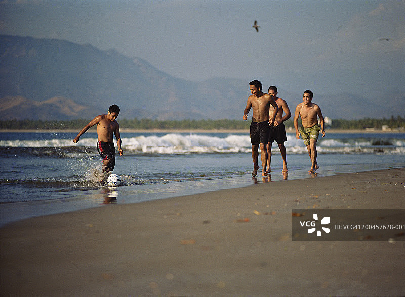 年轻男人在海滩上踢足球图片素材