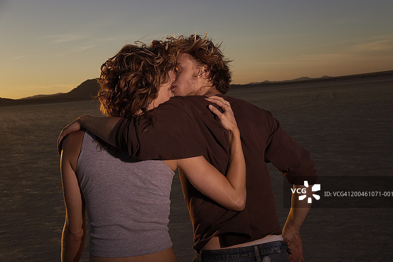 情侣在沙漠中散步，互相搂着手臂，后视图，日落图片素材
