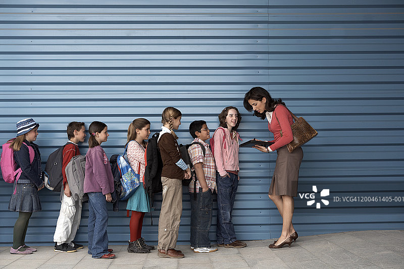 女老师站在一排孩子（8-12岁）旁边，侧视图图片素材