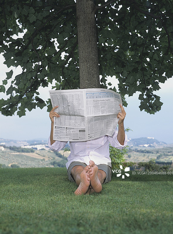 男人坐在树下看报纸特写图片素材
