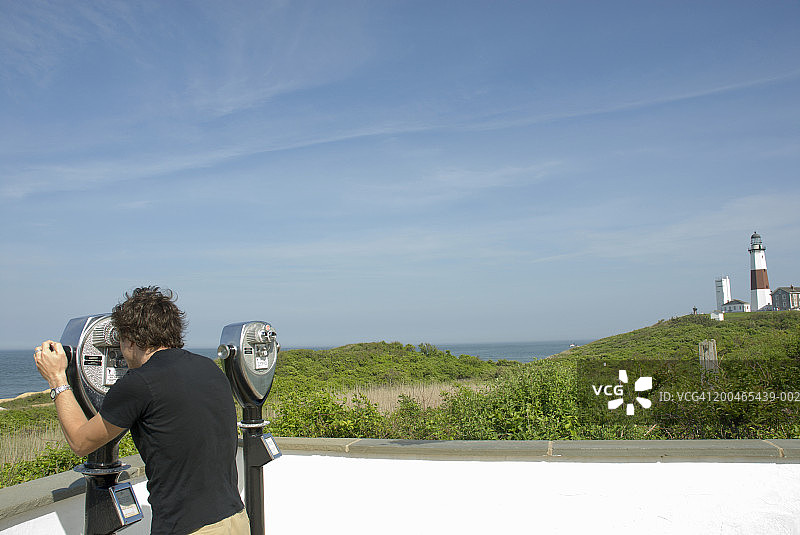 男子通过投币式望远镜观看海景，侧面视角图片素材