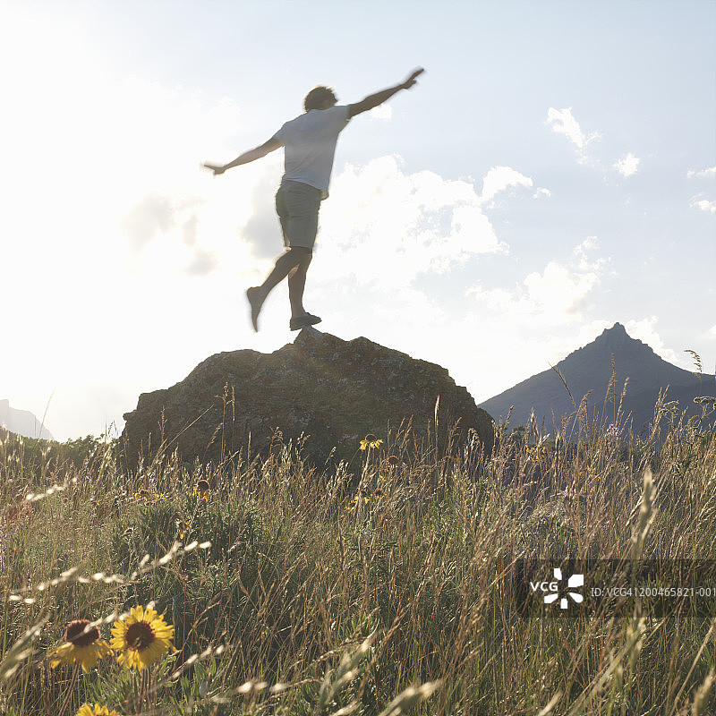 男人在田野里的岩石上保持平衡，低角度视角图片素材