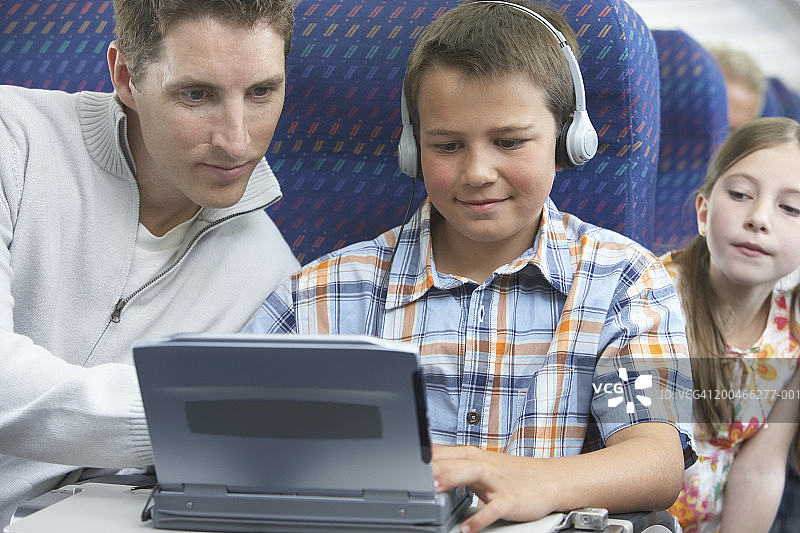 父亲和两个孩子（7-10岁）在飞机上使用笔记本电脑图片素材