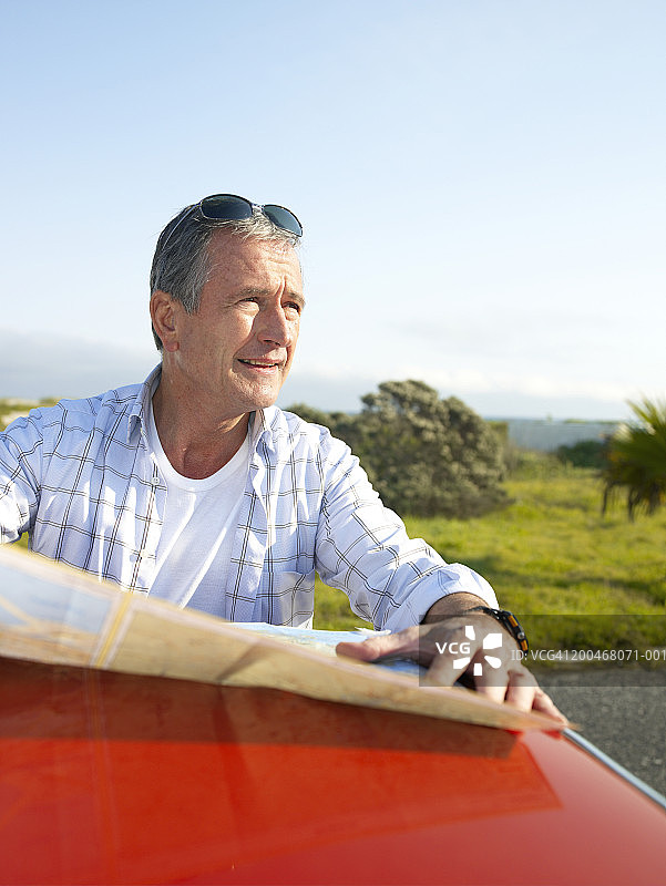 站在汽车旁，靠着车顶看地图的中年男人图片素材