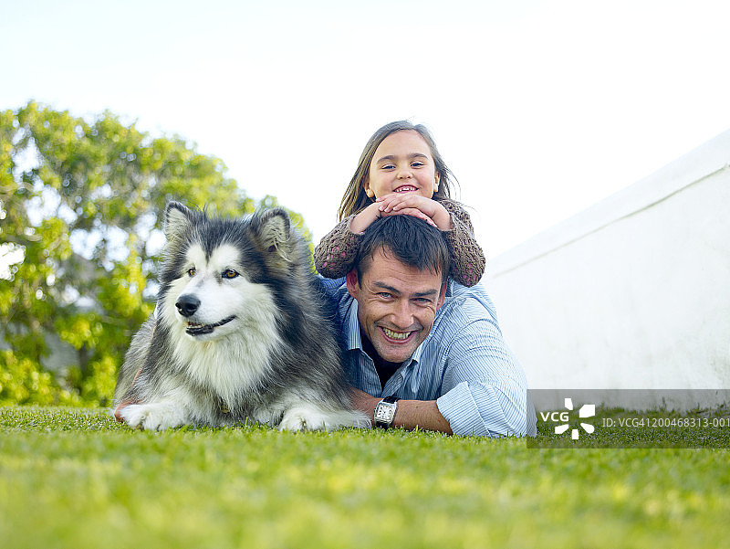 男子躺在草地上，背着女儿（5-7岁），旁边有狗，肖像图片素材