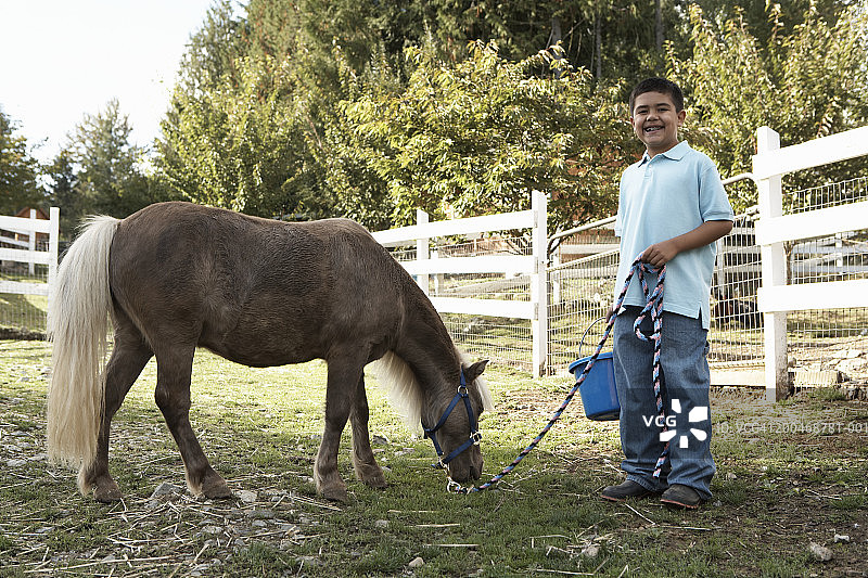 在牧场里设特兰矮种马旁边的男孩（7-9岁）肖像图片素材