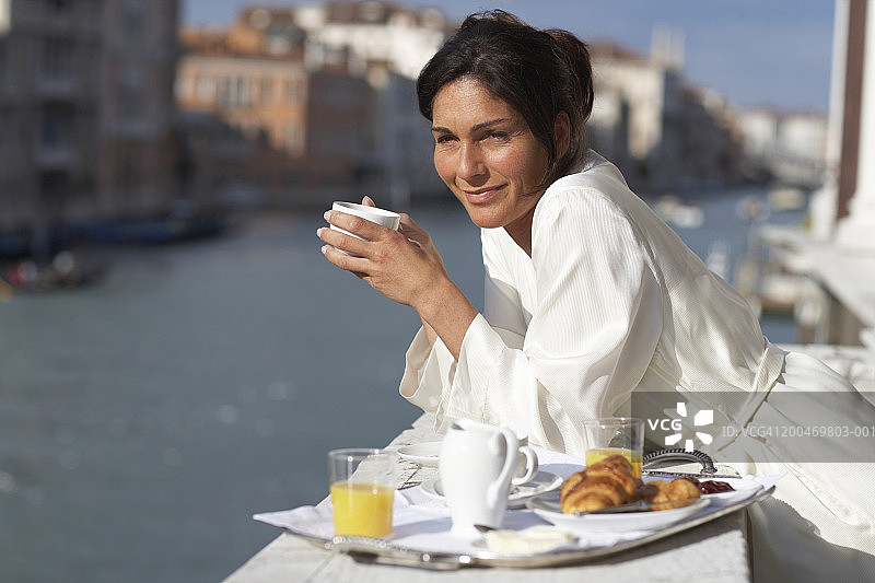 倚靠阳台，在早餐盘旁微笑的女人图片素材