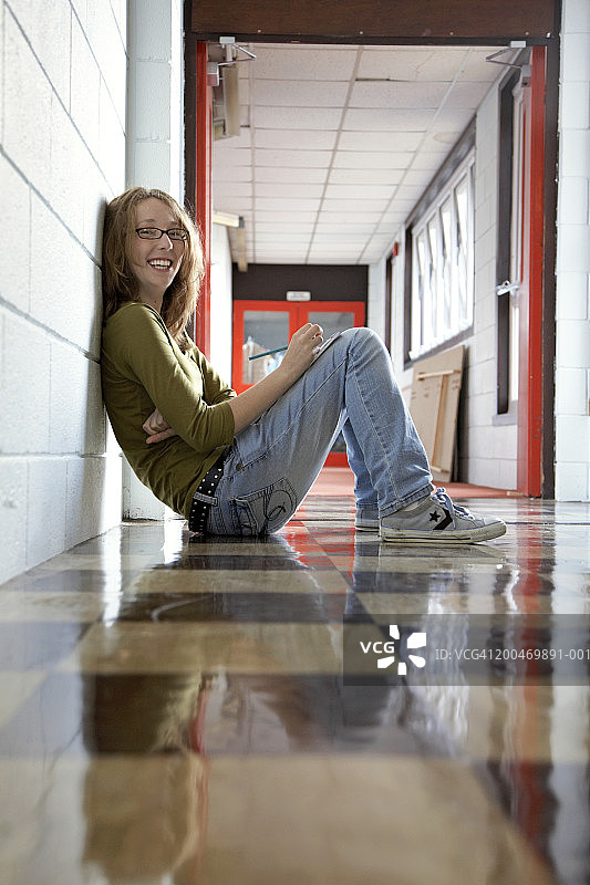 坐在走廊地板上的少女（15-17岁）的微笑肖像图片素材