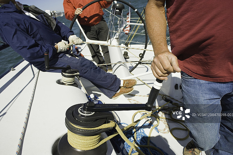 男子在帆船上转动电缆绞盘的手柄，低角度拍摄图片素材
