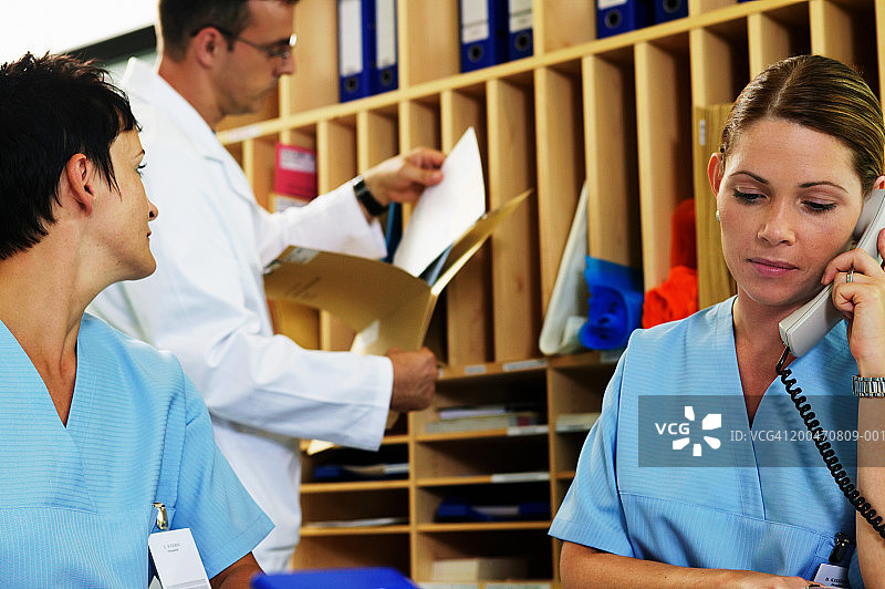 两位在办公桌前的护士，一位正在打电话，另一位回头看着医生图片素材