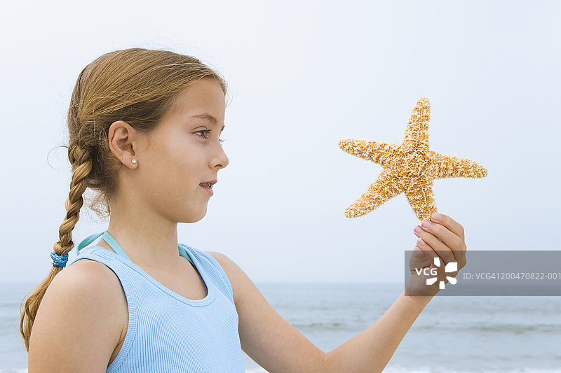 女孩(9-11)在海滩上抱着海星，侧视图图片素材