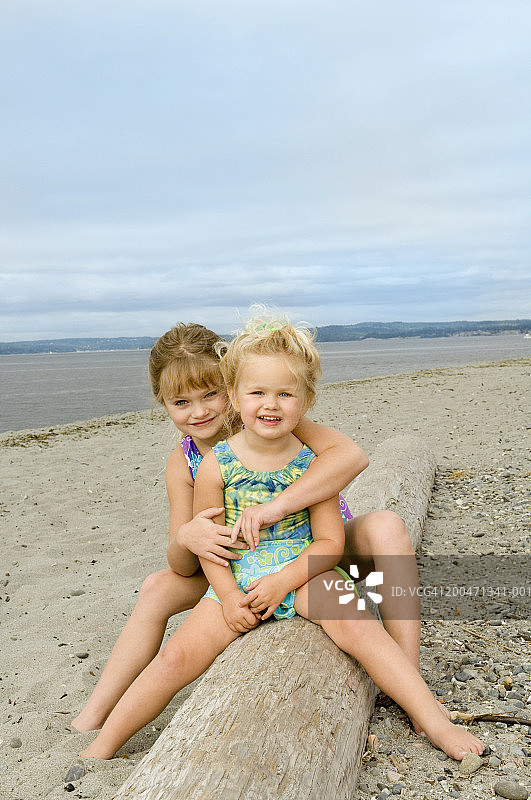 两个坐在海滩浮木上的姐妹（3-6岁）的肖像图片素材