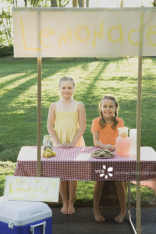 两个女孩（7-10岁）在柠檬水摊旁微笑，特写图片素材