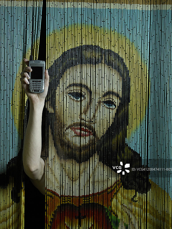 女人透过珠帘拿着手机，屏幕显示耶稣像图片素材