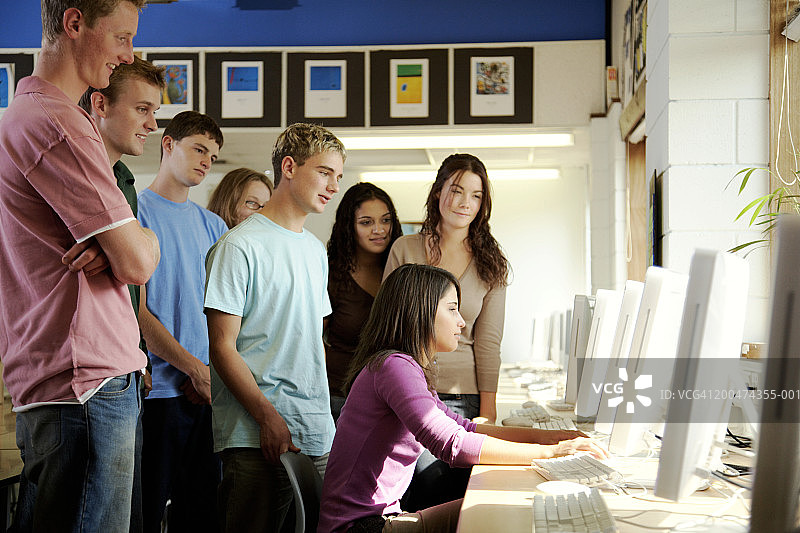 年轻学生看着十几岁的女孩(15-17岁)使用电脑，面带微笑图片素材
