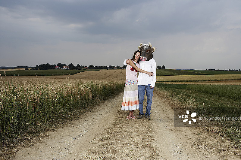 年轻情侣站在田野旁，男人戴着公牛面具图片素材