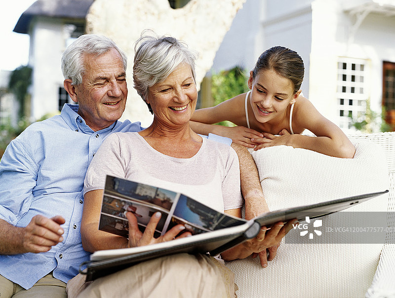祖父母和孙女（12-14岁）一起看相册，面带微笑图片素材