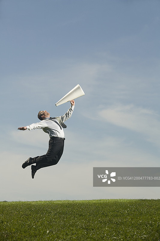 在田野里跳跃并用扩音器讲话的商人图片素材