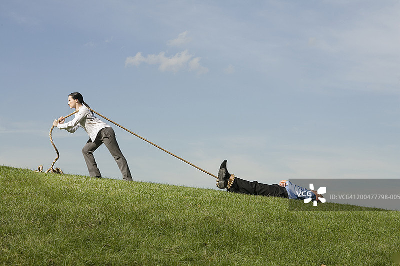 女商人用绳子拖着穿过田野的男商人（侧视图）图片素材