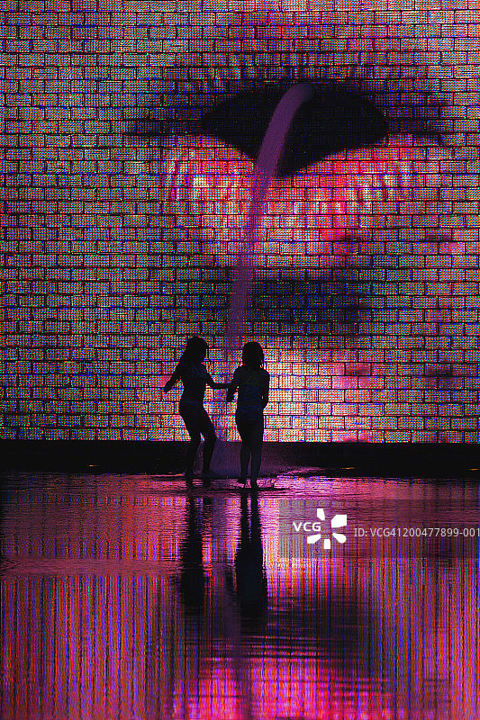 黄昏时分，皇冠喷泉前的两个女孩的轮廓图片素材