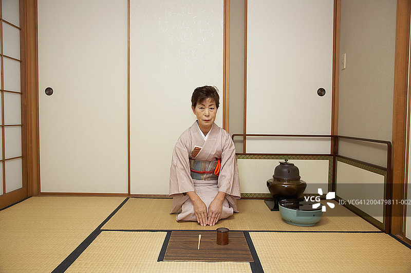 跪在地板上的茶具前方的老年妇女图片素材