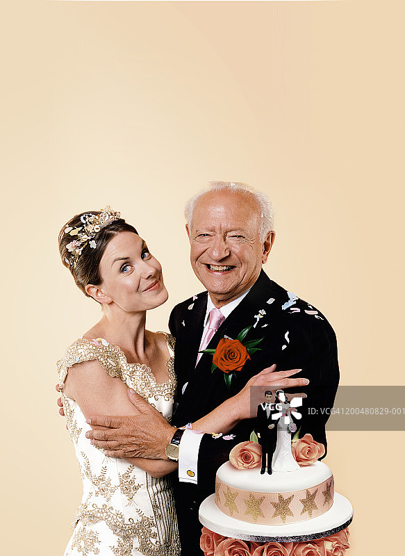 新娘和年长的新郎拥抱在蛋糕旁，微笑，肖像图片素材