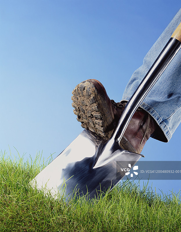 男子用脚将铲子推入草地，特写，低角度图片素材