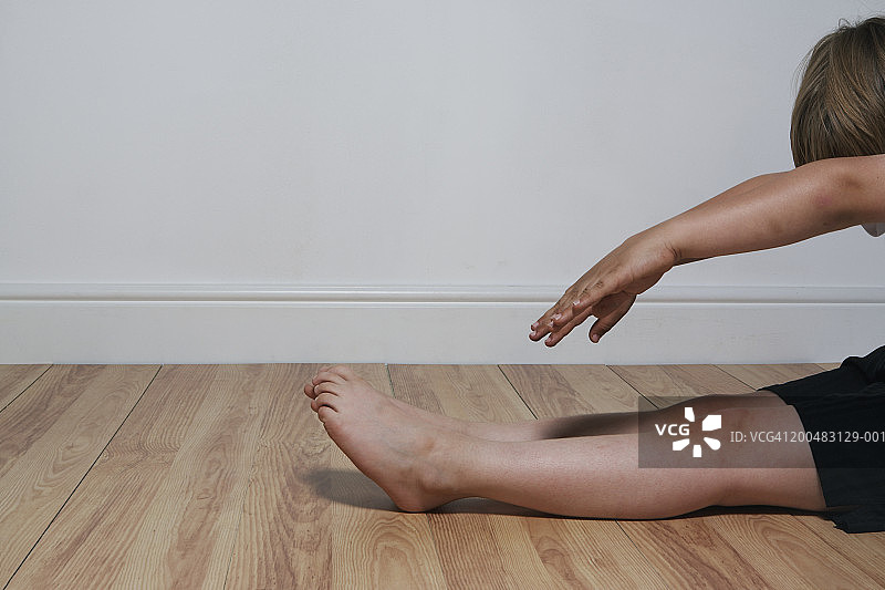 坐在地上伸手触摸脚趾的男孩（6-8岁），侧视图图片素材