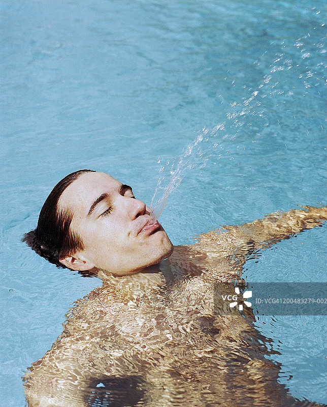 男人漂浮在泳池里，吐水图片素材