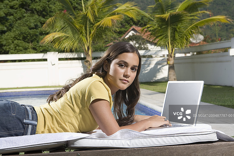 在泳池附近使用笔记本电脑的少女（16-18岁），肖像图片素材