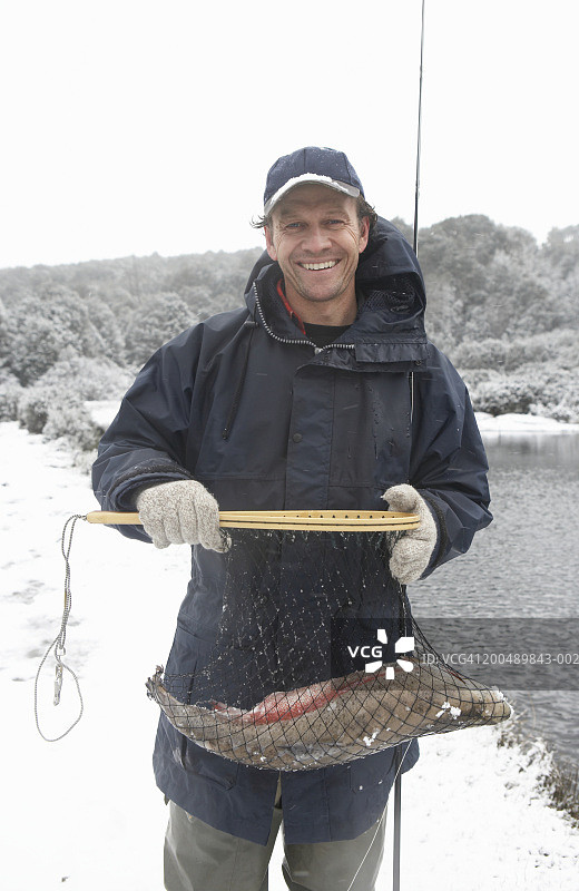 在湖边拿着网兜里的鱼微笑的男人肖像图片素材