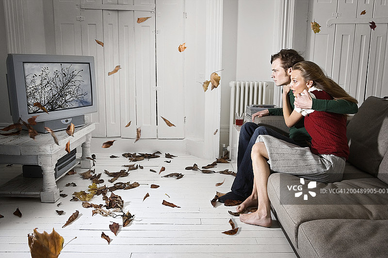 风暴从电视屏幕吹入客厅，情侣正在观看图片素材