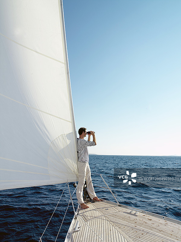 男人站在游艇的船头，使用双筒望远镜图片素材