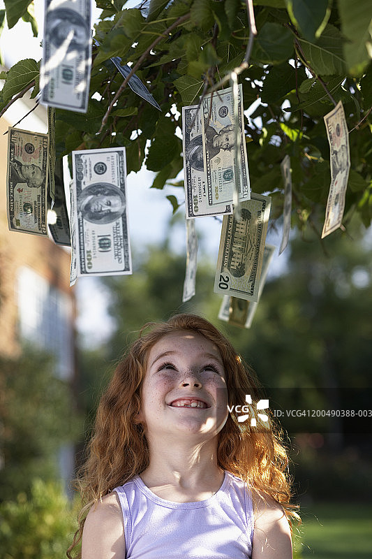 抬头看着树上挂着的钞票的女孩（6-8岁）图片素材