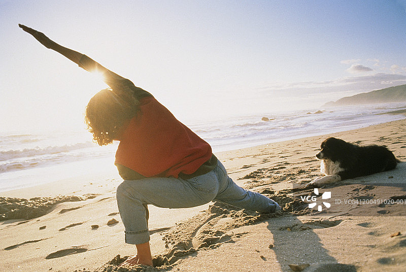 海滩上，女人在狗旁边伸展身体，后视图（镜头光晕，倾斜）图片素材