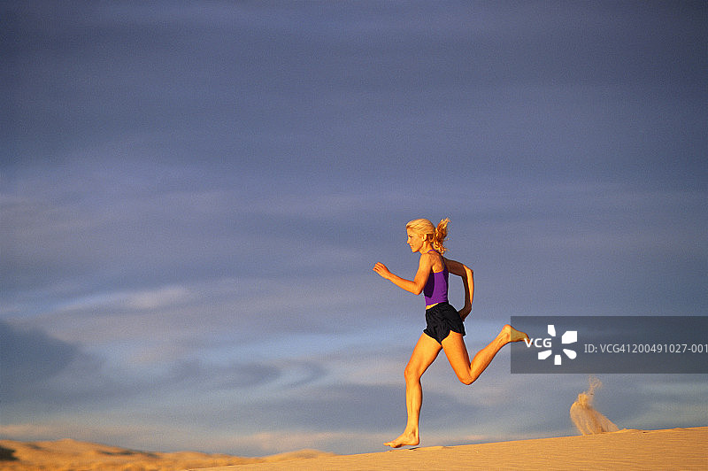 日落时分赤脚在沙丘上慢跑的女子，侧面轮廓图片素材