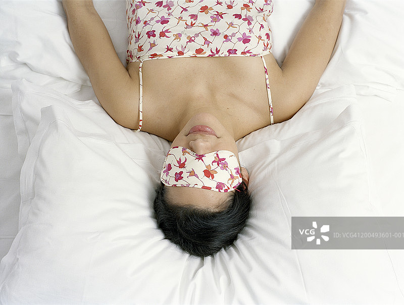 年轻女人躺在床上，戴着睡眠眼罩，高角度拍摄图片素材