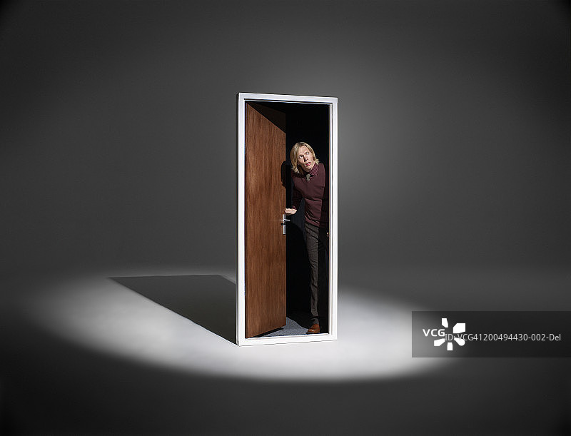 男子站在聚光灯下的独立门框中向外看图片素材