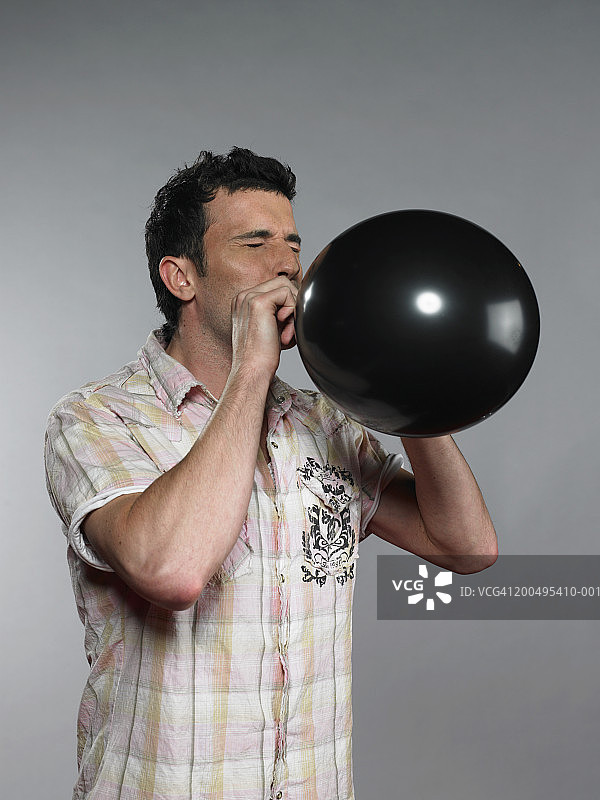 男子闭着眼睛吹黑色气球图片素材