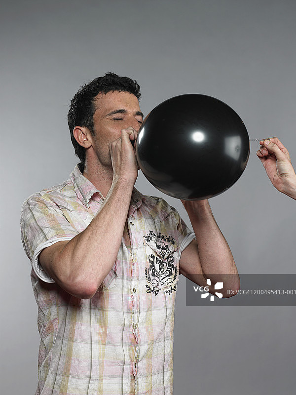 男人吹黑色气球，另一个人拿着针要扎破它图片素材