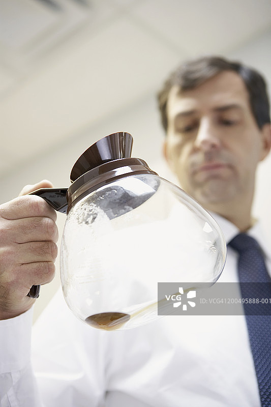 中年商人拿着空咖啡壶在办公室厨房图片素材