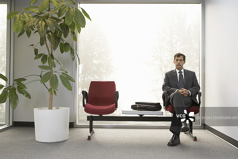 中年商人坐在大厅里，双手合十图片素材