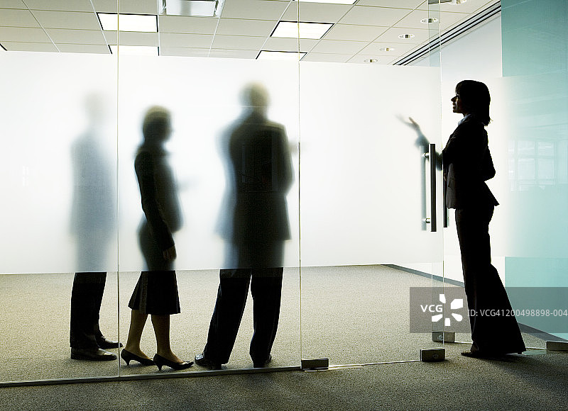 三个同事站在磨砂玻璃后，一名女子走进办公室图片素材