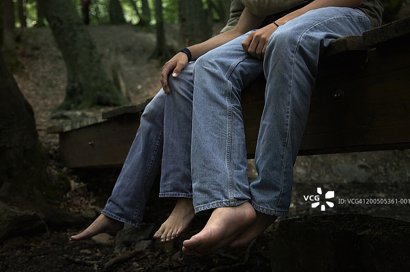 年轻夫妇坐在木桥上，手放在腿上，低角度拍摄图片素材