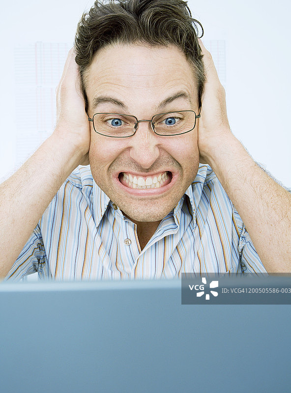 捂着耳朵使用笔记本电脑的中年男人，特写镜头图片素材